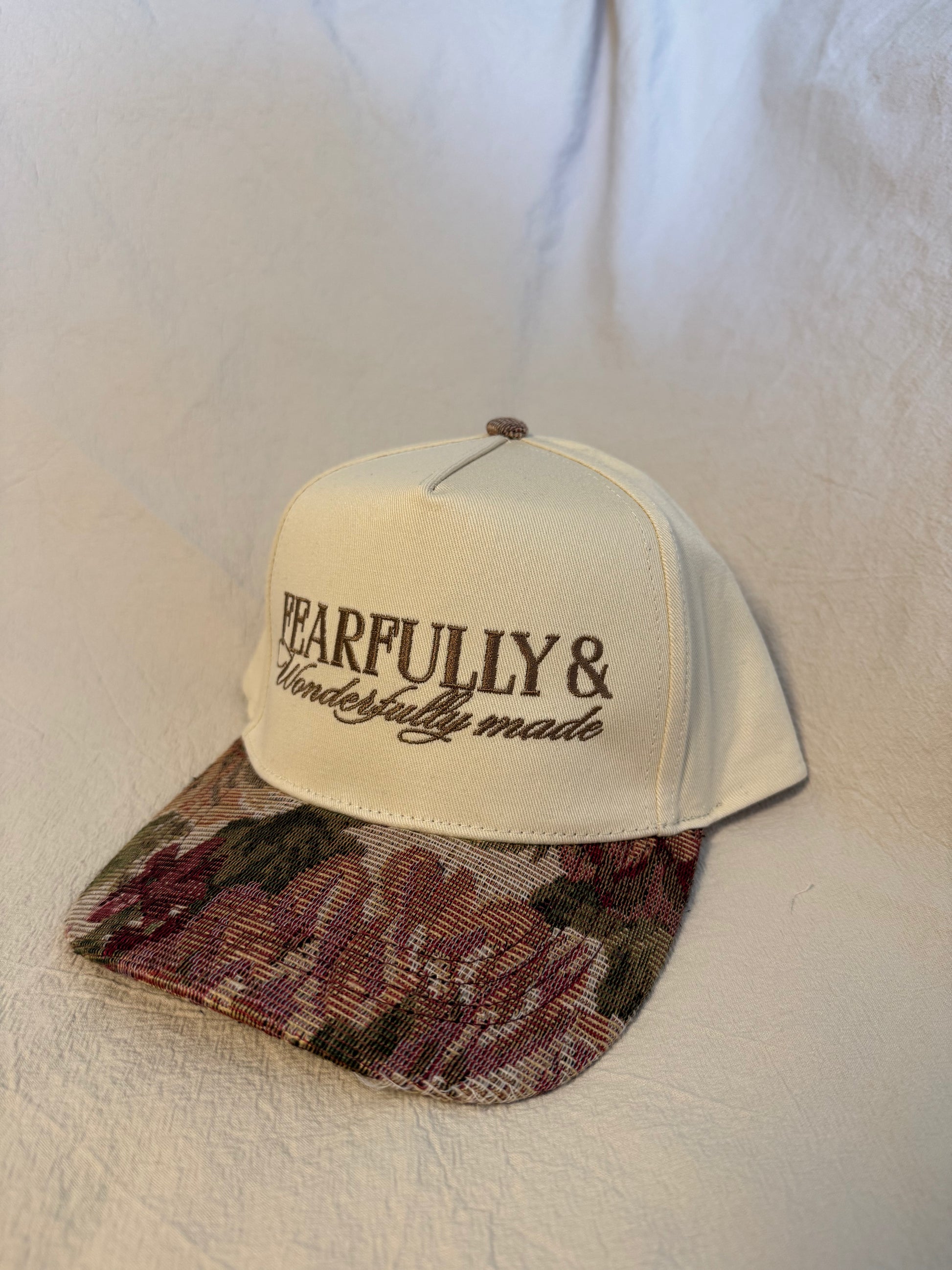 A baseball cap with an off-white crown and a floral-patterned visor, featuring the embroidered text 'FEARFULLY & Wonderfully made' on the front, displayed against a textured off-white fabric background.
