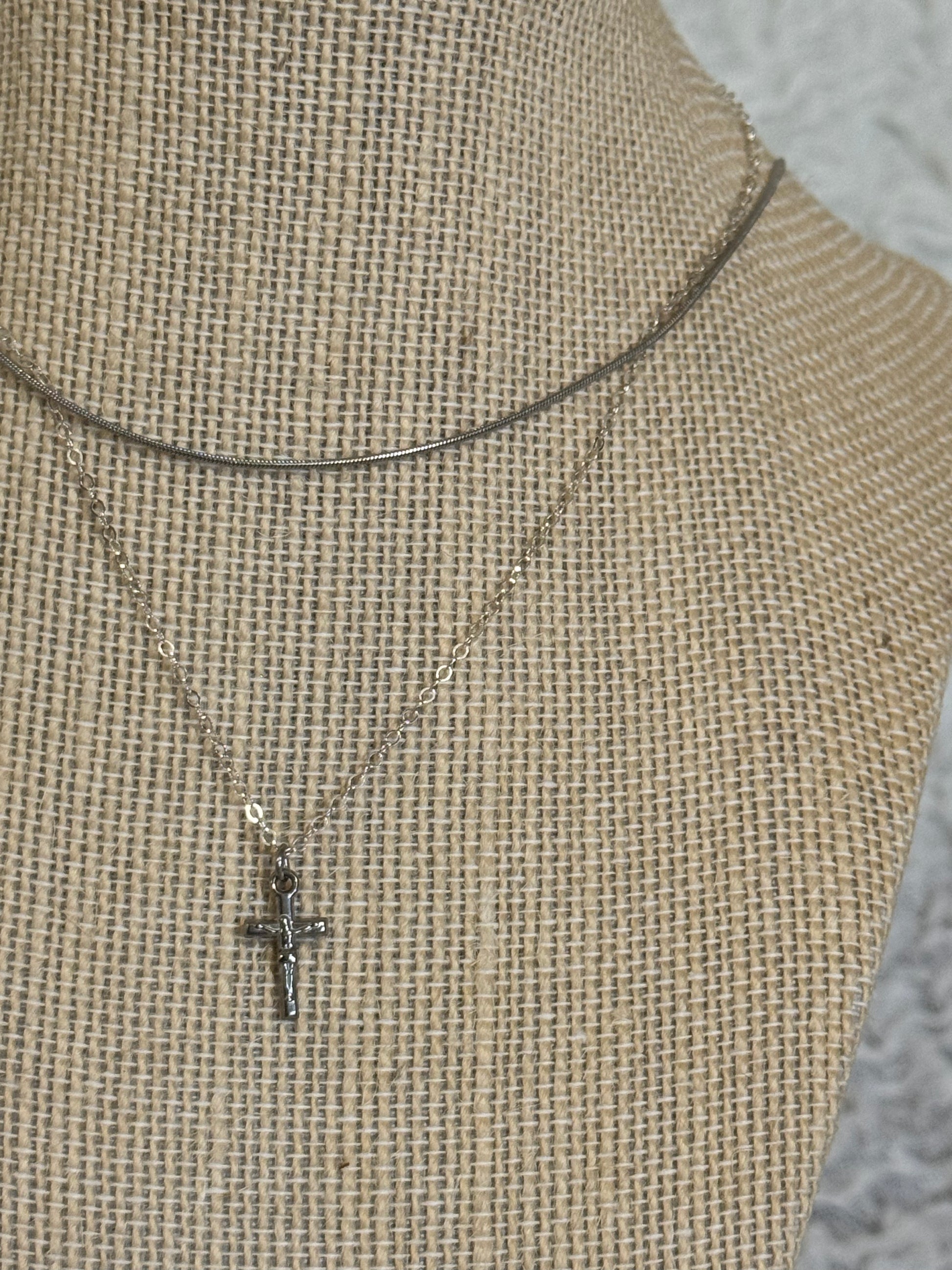 Close up of dainty stainless steel crucifix pendant on sterling silver chain